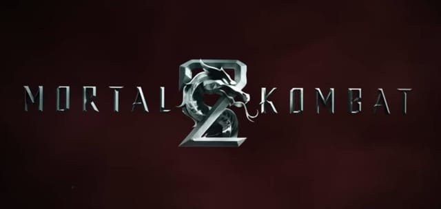 Logotipo oficial do filme Mortal Kombat 2 de 2026, com o título em letras prateadas texturizadas e o icônico dragão metálico no centro. O fundo é uma superfície texturizada vermelha escura e profunda.