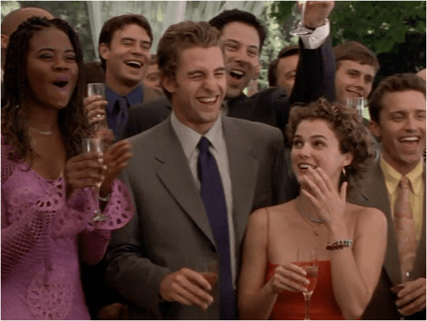 Atores do elenco da série Felicity brindando e sorrindo com taças de champanhe em um momento de celebração. Em destaque, Keri Russell exibe o seu polêmico corte de cabelo curto.