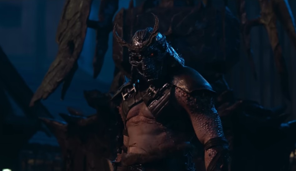 Shao Kahn (interpretado por Martyn Ford) em Mortal Kombat 2 (2026), vestindo seu icônico capacete de caveira com chifres e olhos vermelhos brilhantes. O vilão aparece em um ambiente sombrio com iluminação azul, destacando sua armadura de batalha e seu físico massivo e imponente.